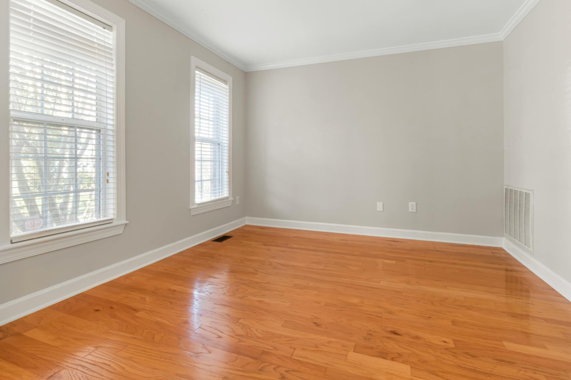 Empty room in a McKinney, Texas, home featuring honey-toned hardwood floors with visible grain, white trim, and natural light from double windows.
